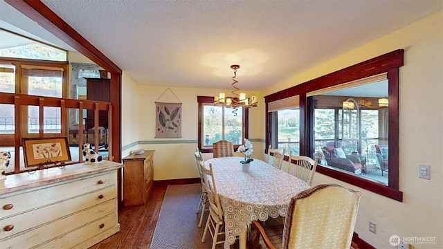dining space with a textured ceiling, dark wood-style flooring, baseboards, and an inviting chandelier