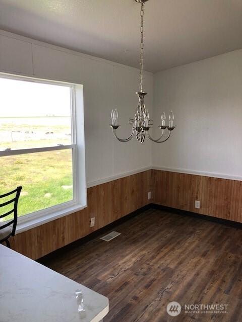 unfurnished dining area with visible vents, wainscoting, an inviting chandelier, and dark wood-type flooring