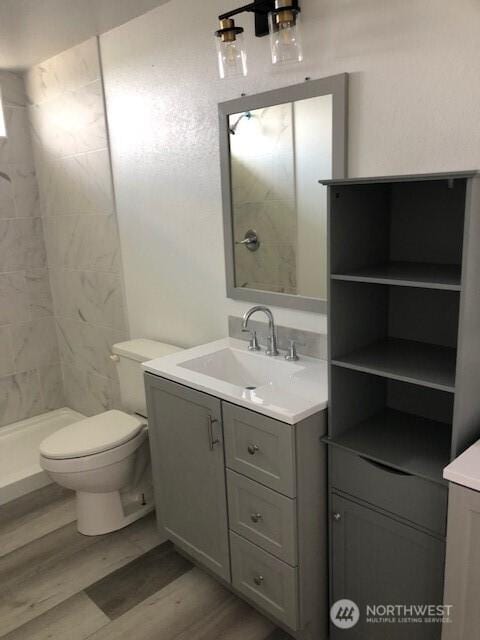bathroom with vanity, wood finished floors, toilet, and a shower stall