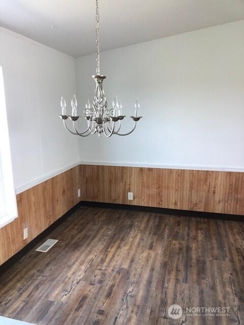 unfurnished dining area featuring wainscoting, dark wood-style flooring, a chandelier, and visible vents