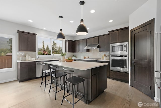 kitchen featuring light countertops, dark brown cabinets, appliances with stainless steel finishes, and under cabinet range hood