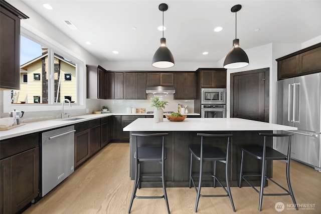 kitchen with dark brown cabinetry, a sink, a center island, and appliances with stainless steel finishes