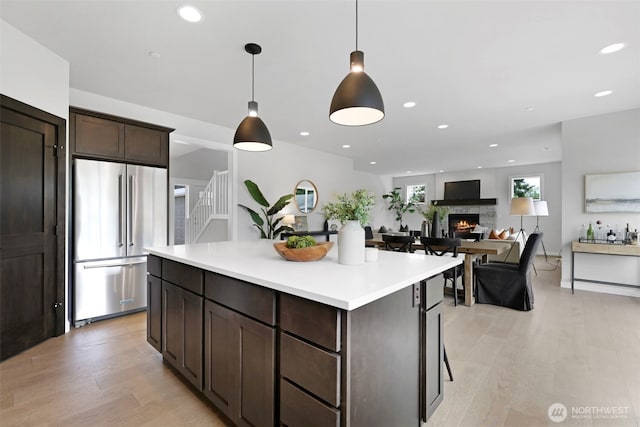 kitchen with high end fridge, a lit fireplace, light wood-type flooring, and dark brown cabinetry