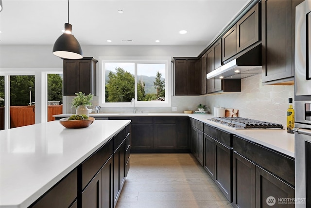 kitchen with decorative backsplash, light countertops, dark brown cabinets, under cabinet range hood, and a sink