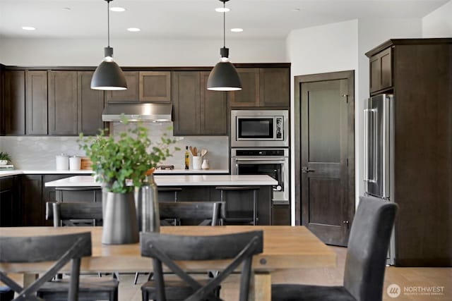 kitchen with light countertops, stainless steel appliances, under cabinet range hood, and dark brown cabinetry