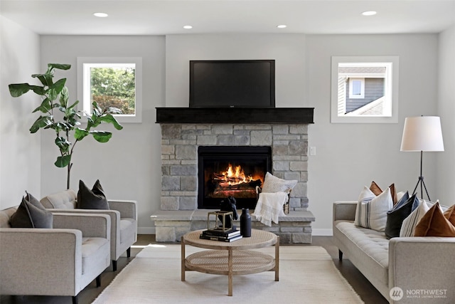 living area with recessed lighting, a stone fireplace, baseboards, and wood finished floors