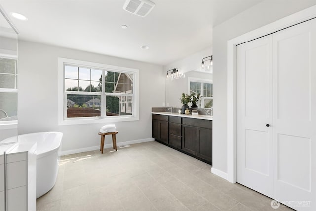 full bathroom with visible vents, a soaking tub, baseboards, double vanity, and a sink