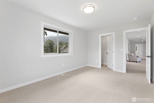 unfurnished bedroom featuring a closet, visible vents, baseboards, a spacious closet, and light colored carpet