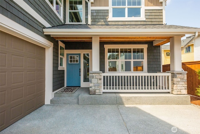 view of exterior entry with concrete driveway, covered porch, and roof with shingles