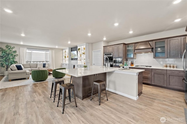 22819 SE Fir St, Black Diamond, WA 98010 - kitchen with light wood-style floors, custom exhaust hood, light countertops, a center island with sink, and a breakfast bar area
