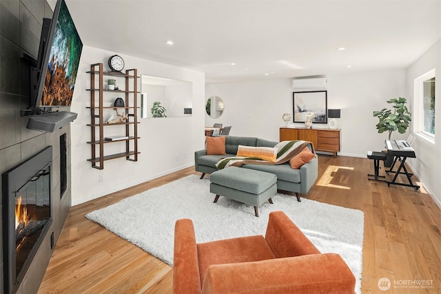 living room with baseboards, light wood-style floors, a glass covered fireplace, and a wall mounted air conditioner