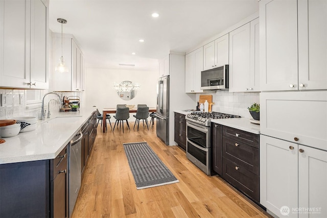 kitchen with white cabinetry, decorative backsplash, stainless steel appliances, light wood finished floors, and a sink