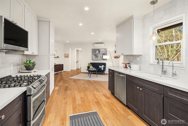 kitchen featuring tasteful backsplash, light wood-type flooring, light countertops, stainless steel appliances, and a sink