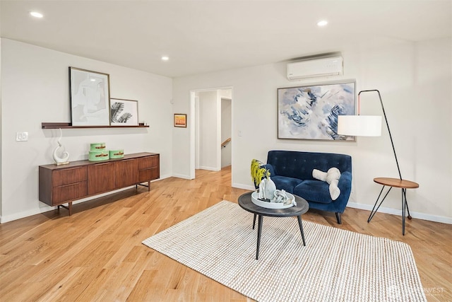 sitting room with an AC wall unit, baseboards, light wood-type flooring, and recessed lighting