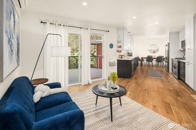 living room with a wall mounted air conditioner, recessed lighting, and light wood-style flooring