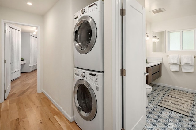 washroom featuring laundry area, visible vents, stacked washing maching and dryer, light wood finished floors, and baseboards