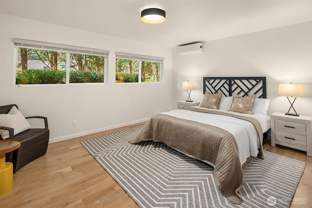 bedroom featuring a wall mounted AC, light wood-style flooring, and baseboards