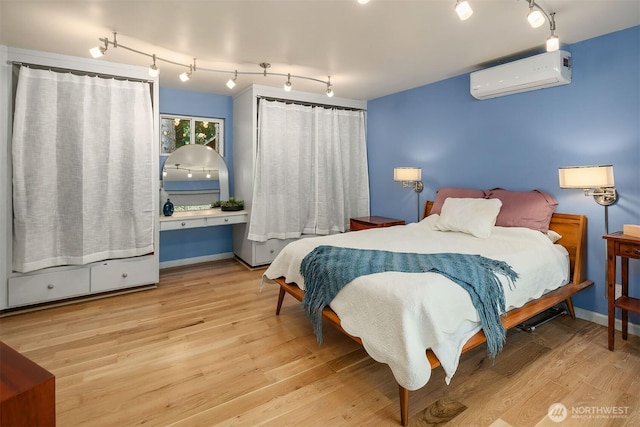 bedroom featuring track lighting, baseboards, a wall unit AC, and wood finished floors