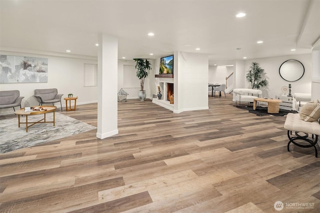 living area with a lit fireplace, recessed lighting, stairway, wood finished floors, and baseboards