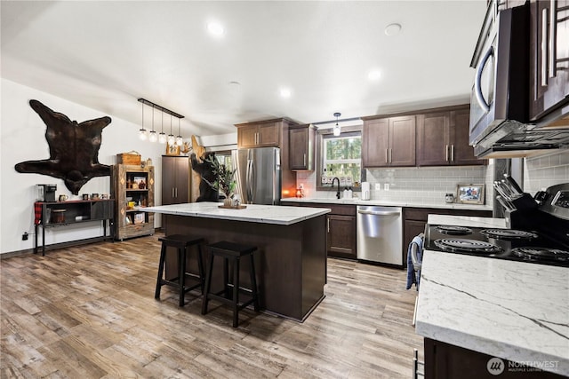14205 205th Street Ct E, Graham, WA 98338 - kitchen with light wood finished floors, a breakfast bar, a center island, tasteful backsplash, and appliances with stainless steel finishes