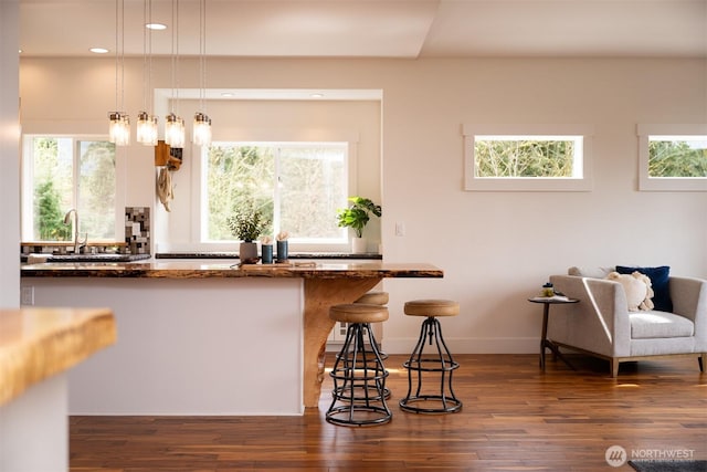kitchen with hanging light fixtures, baseboards, a sink, a kitchen bar, and wood finished floors