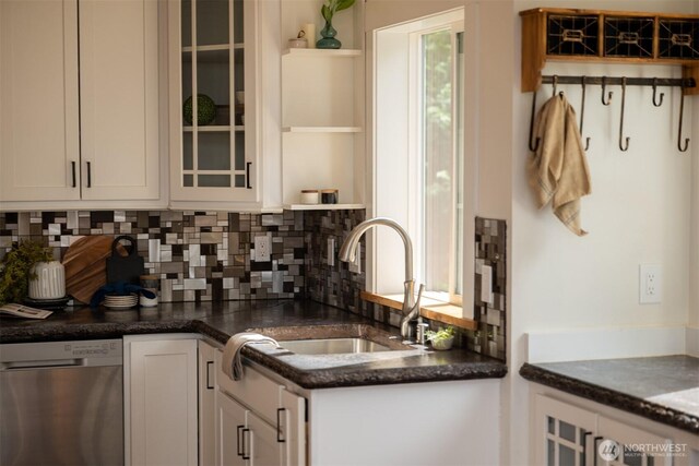 kitchen with glass insert cabinets, white cabinets, dishwasher, a sink, and backsplash