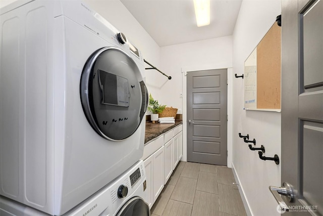 clothes washing area with cabinet space, baseboards, and stacked washer / drying machine