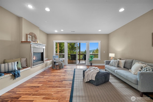 living area featuring recessed lighting, wood finished floors, a glass covered fireplace, and baseboards