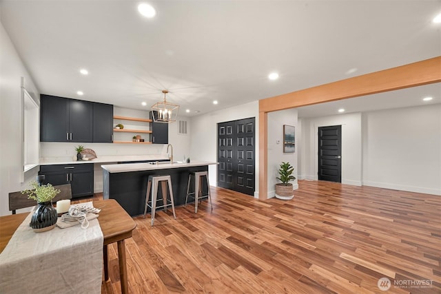 kitchen with an island with sink, light wood-type flooring, open shelves, light countertops, and a breakfast bar area