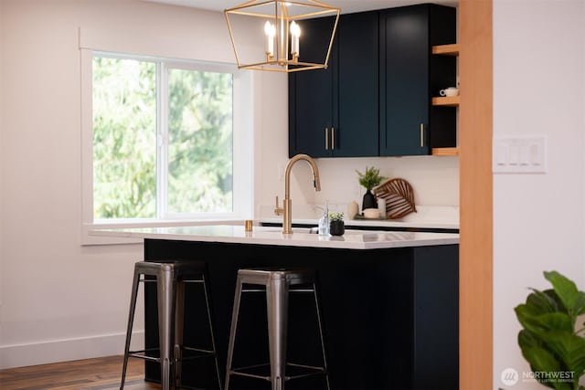 kitchen featuring an inviting chandelier, open shelves, wood finished floors, light countertops, and a breakfast bar area
