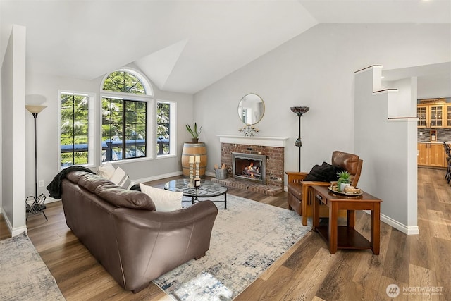 living area featuring a fireplace, baseboards, wood finished floors, and lofted ceiling