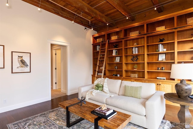 living room featuring dark wood-type flooring, rail lighting, baseboards, and beamed ceiling