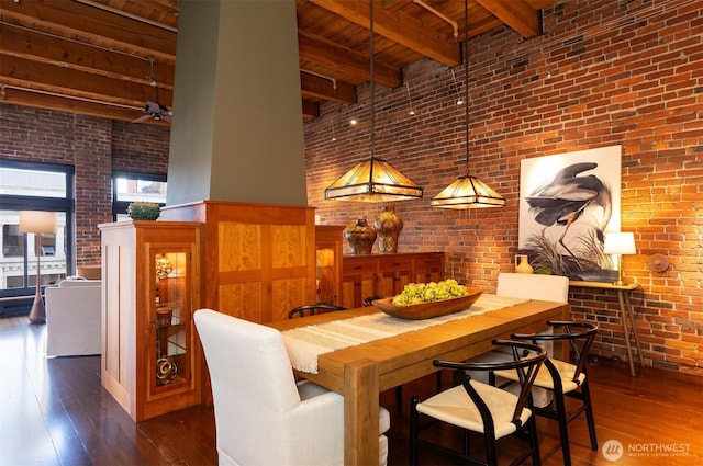 dining space with wood-type flooring, a high ceiling, beamed ceiling, and brick wall
