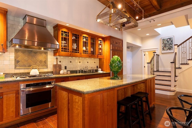kitchen with brown cabinets, dark wood-style flooring, exhaust hood, and stainless steel appliances