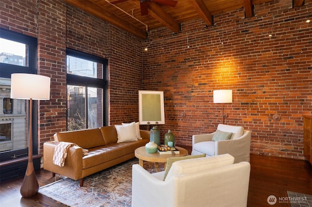 living room featuring beam ceiling, wood ceiling, a high ceiling, wood finished floors, and brick wall