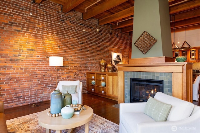 living room with wood ceiling, brick wall, beamed ceiling, a tile fireplace, and wood finished floors