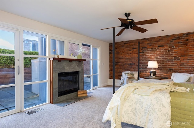 carpeted bedroom featuring a fireplace with flush hearth, access to outside, brick wall, visible vents, and ceiling fan