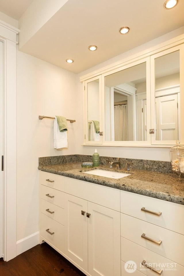 bathroom with baseboards, wood finished floors, recessed lighting, and vanity