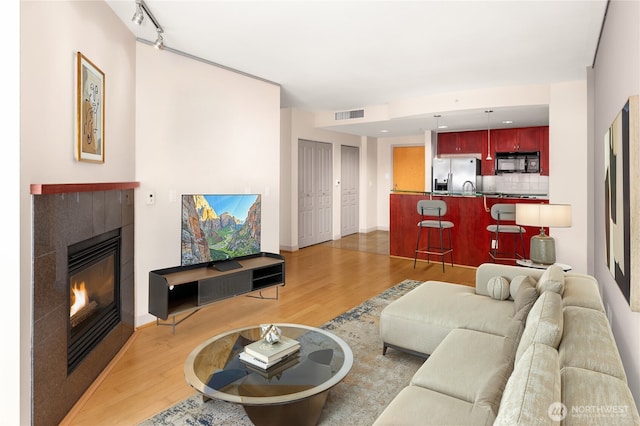 living area featuring light wood-style flooring, track lighting, visible vents, a tile fireplace, and baseboards