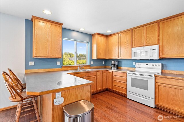 kitchen featuring white appliances, a sink, a kitchen breakfast bar, a peninsula, and wood finished floors
