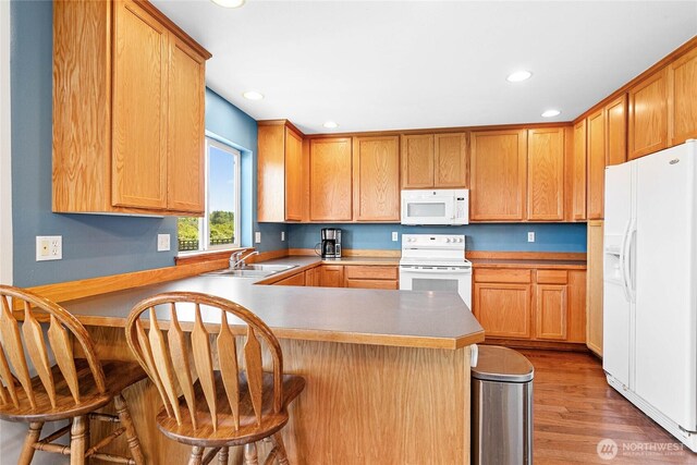 kitchen with white appliances, a sink, a peninsula, light wood-type flooring, and recessed lighting