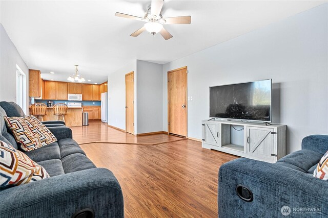 living room featuring a chandelier, light wood finished floors, ceiling fan, and baseboards