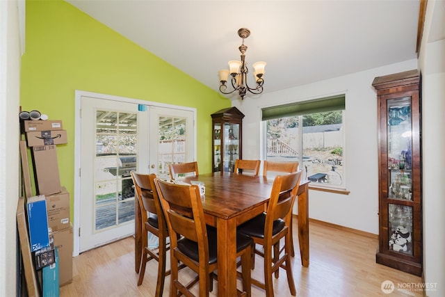 dining area featuring vaulted ceiling, an inviting chandelier, french doors, and light wood-type flooring