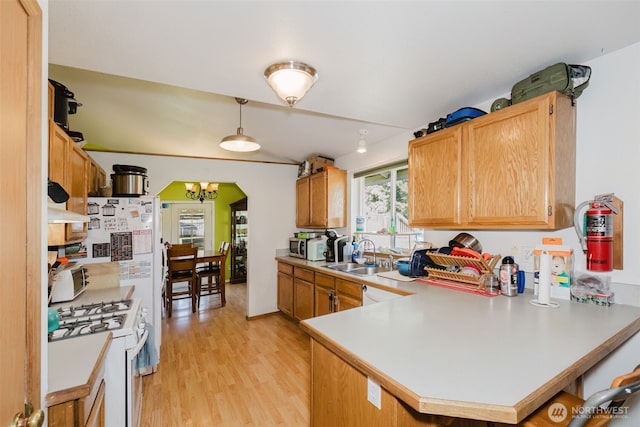 kitchen with light countertops, a sink, light wood-style floors, a peninsula, and white gas range oven