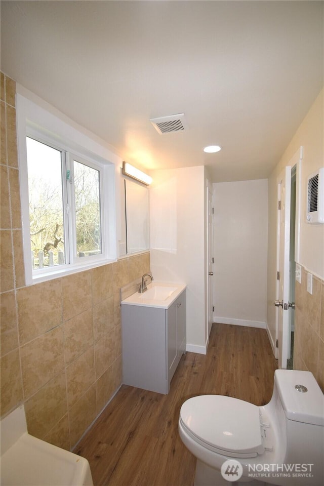 bathroom featuring toilet, vanity, wood finished floors, visible vents, and tile walls