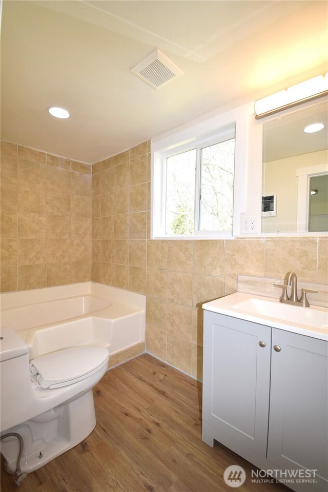 full bath with tile walls, toilet, a bathtub, visible vents, and wood finished floors