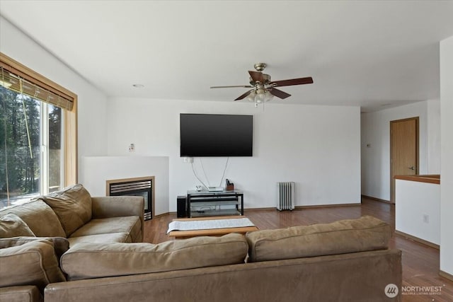 living room with radiator, a fireplace, wood finished floors, and a ceiling fan