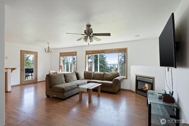 living area featuring ceiling fan with notable chandelier, a glass covered fireplace, and wood finished floors