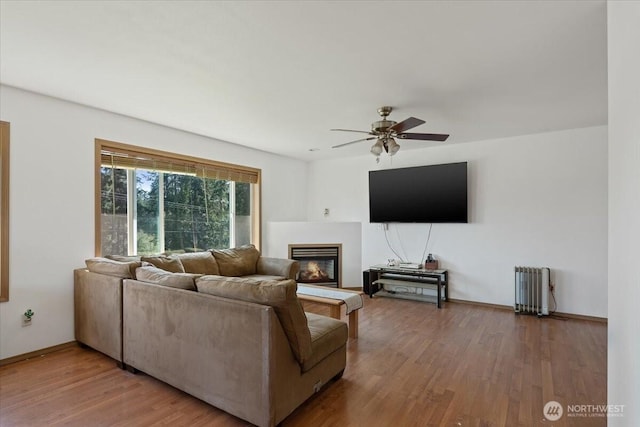 living area with baseboards, wood finished floors, radiator heating unit, a ceiling fan, and a glass covered fireplace