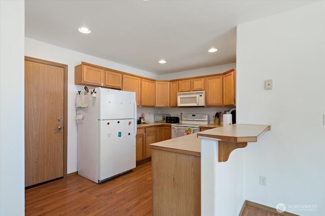 kitchen featuring light countertops, a peninsula, light wood finished floors, white appliances, and a kitchen bar